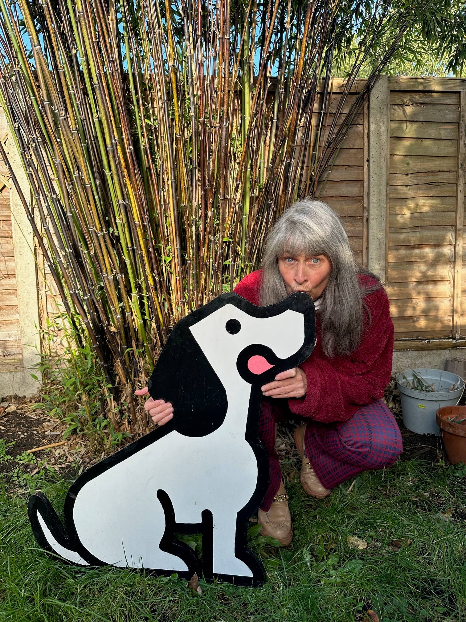 Person holding a large black and white dog-shaped sign in a garden setting.
